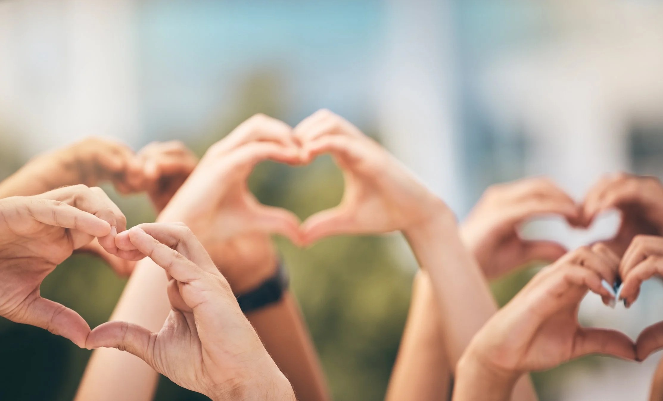 Several pairs of hands forming heart shapes outdoors